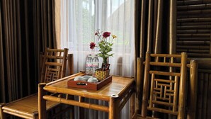 A bamboo table with chairs, a vase with flowers, and a tray with bottles and snacks. - KST Linh Ky Moc (Quang Phu)