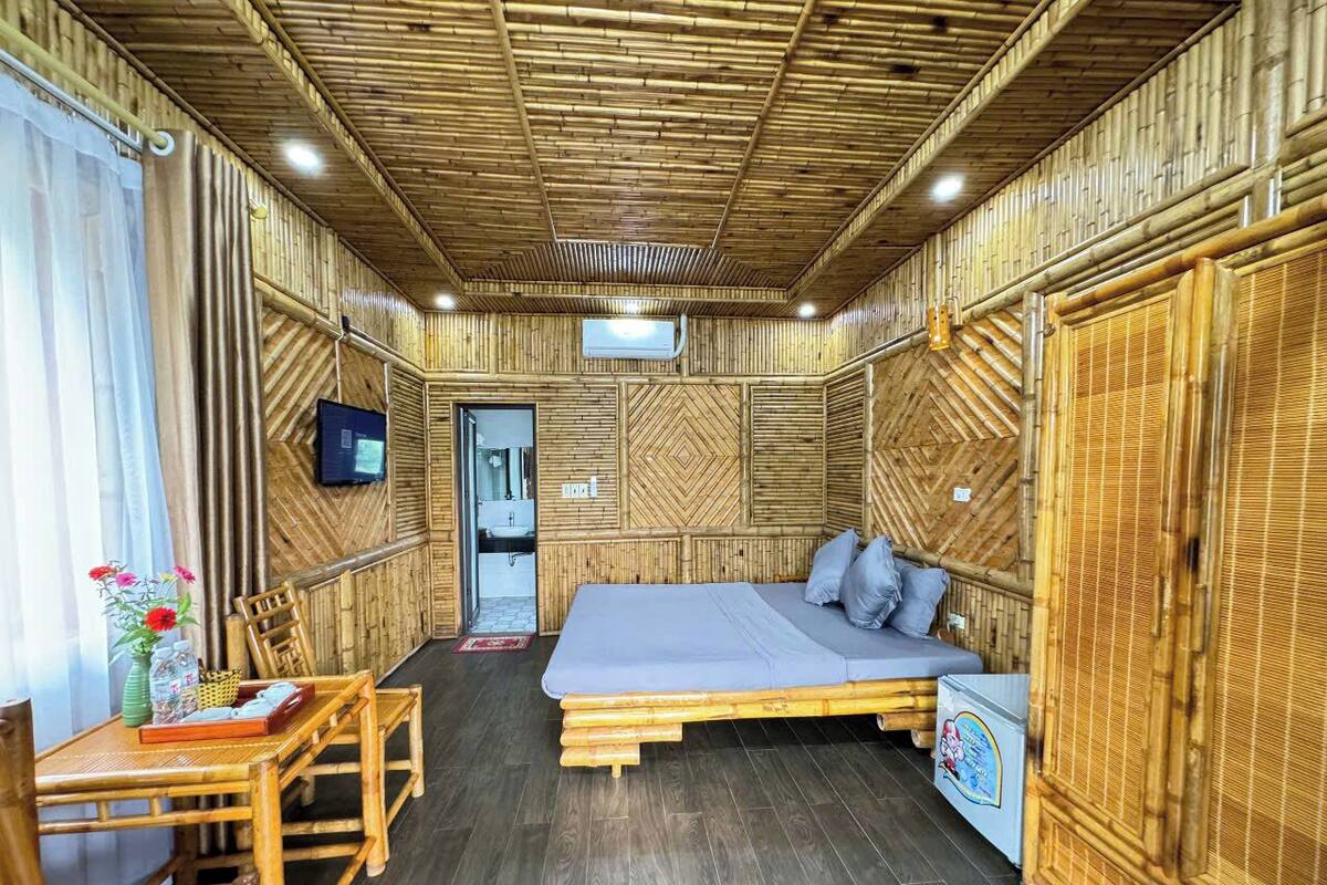 A room with a bed, a table with chairs, a small fridge, and a TV on the wall.