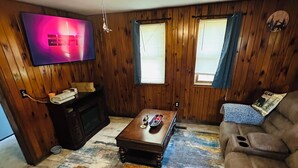 Een woonkamer met houten wanden, een plafondventilator, een flatscreen-televisie, een salontafel, een bank en een vloerkleed.
