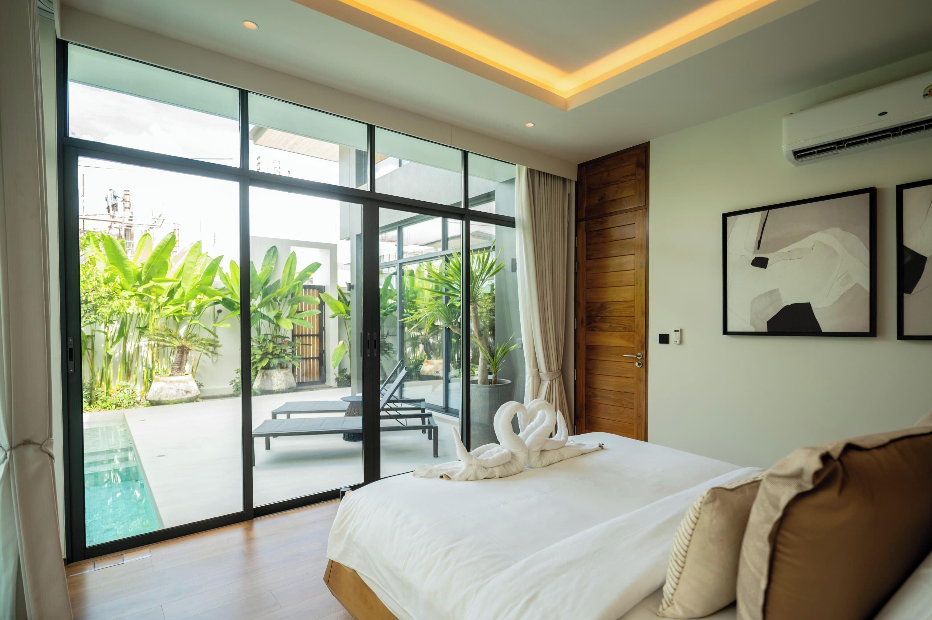 A modern hotel room with a large bed, a glass door leading to a pool area, and a wooden wall.