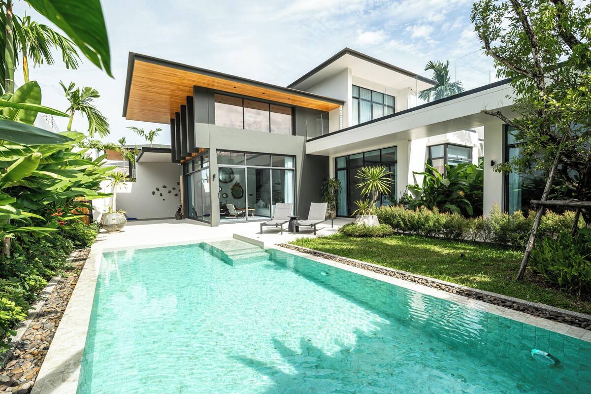 A modern house with a swimming pool, a covered patio, and lush greenery.