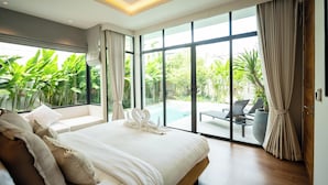 Una habitación de hotel moderna con una cama grande, un sofá y vistas a una piscina y follaje exuberante.