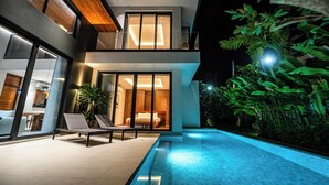 Una casa moderna de dos pisos con piscina, ventanas amplias y un balcón.