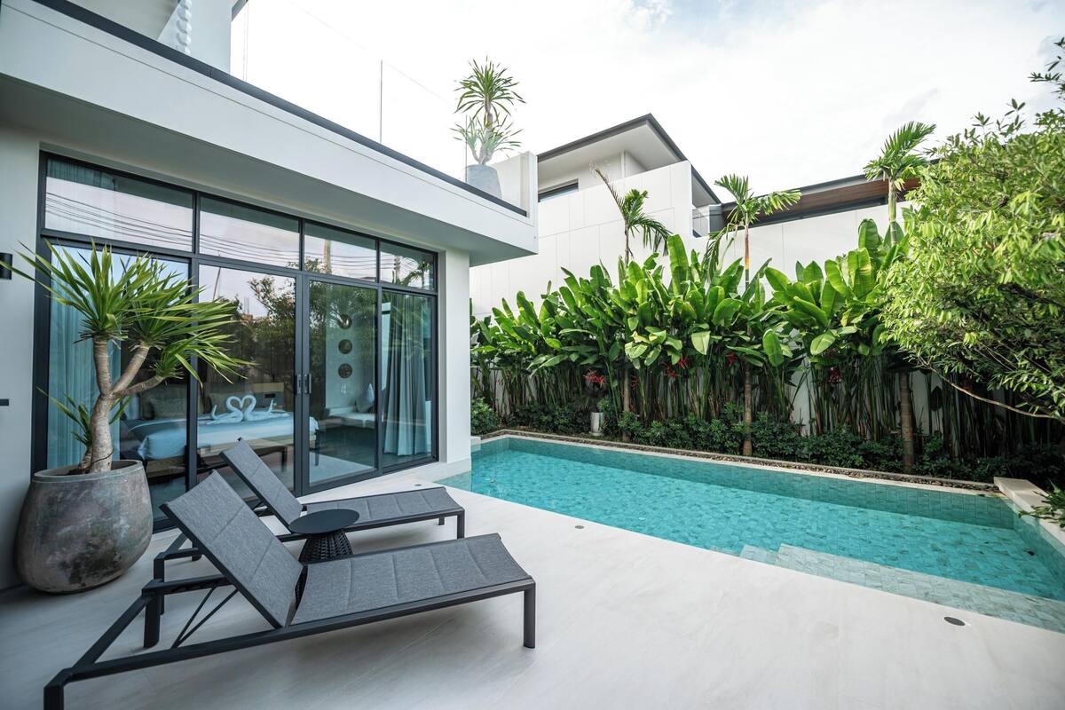 A modern house with a swimming pool, large windows, and a patio with lounge chairs.