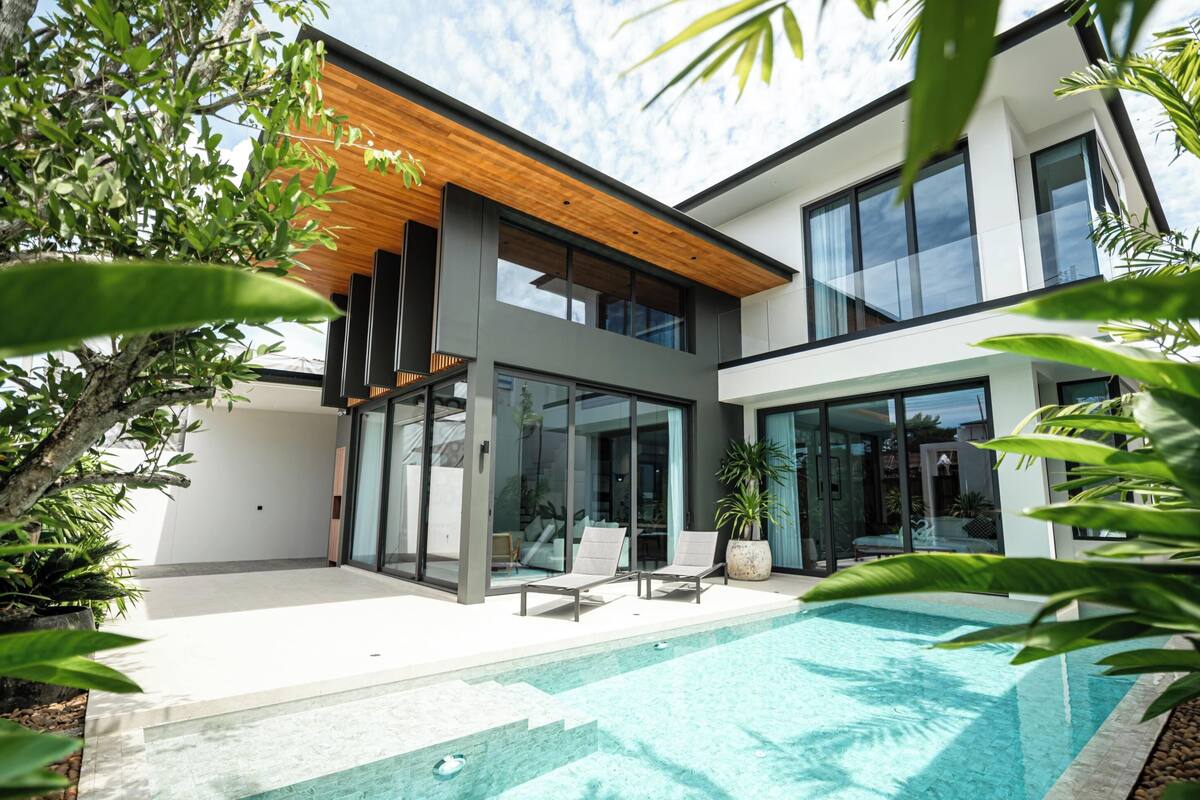 A modern house with a swimming pool, large windows, and a wooden ceiling.
