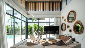 Una sala de estar moderna con un televisor grande, asientos cómodos y vistas a una piscina y vegetación.