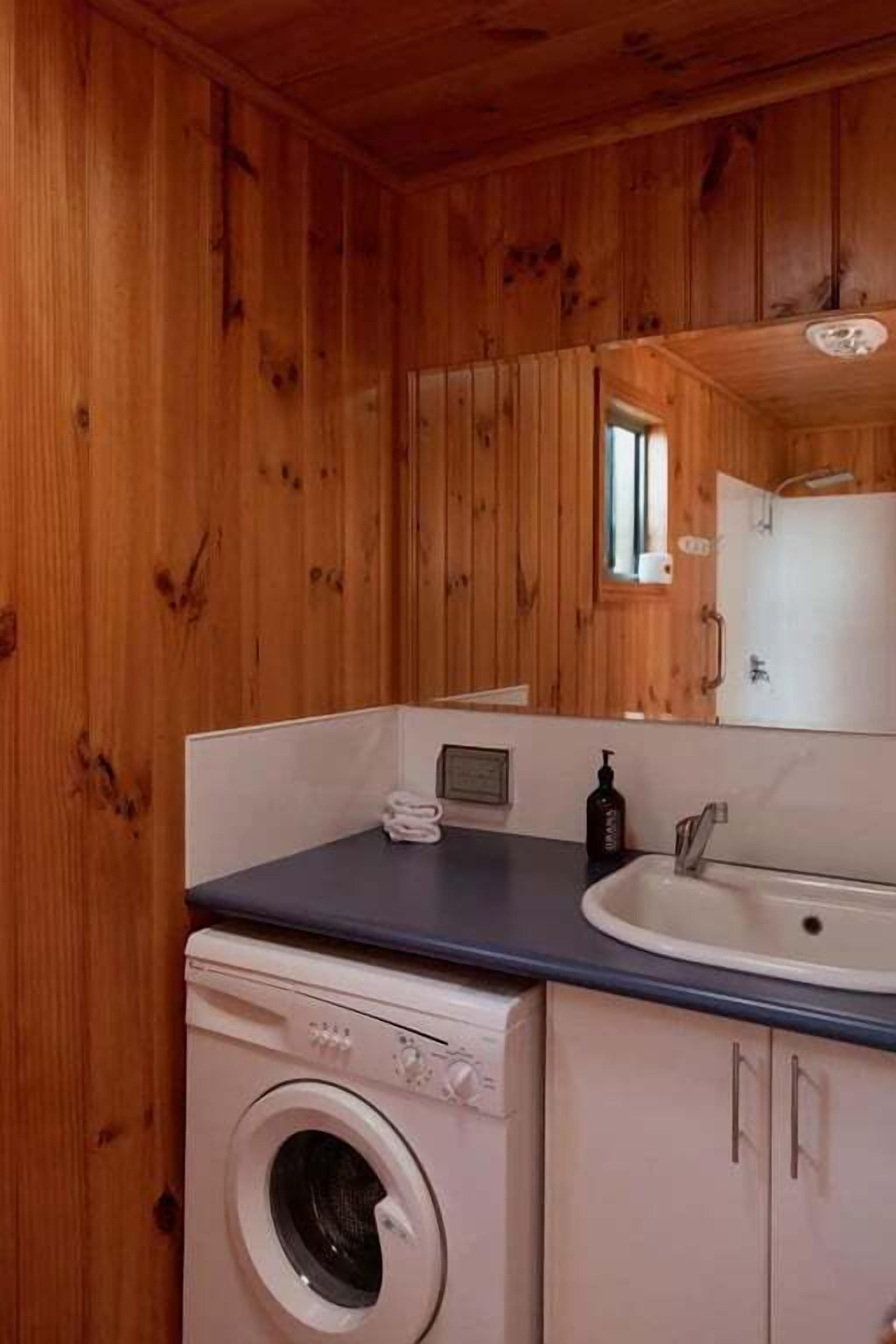 Ett litet badrum med träpanel på väggarna, utrustat med tvättmaskin, handfat och skåp.