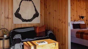 A cozy room with a wooden wall, a black and white striped sofa, a wooden chest, and a bed with a plaid blanket. - Panorama Cabin - a cosy shack and an epic view (A) (Bicheno)