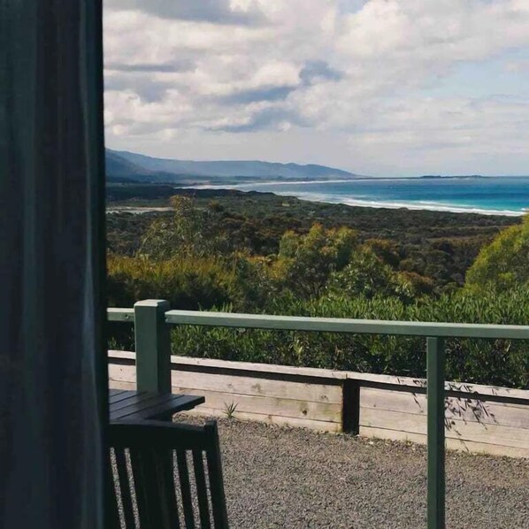 A balcony with a view of a coastal landscape, including a beach and distant mountains.