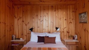 A wooden-paneled room with a bed, two nightstands, and a framed picture on the wall. - Panorama Cabin - a cosy shack and an epic view (A) (Bicheno)