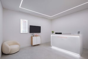 A reception desk with a sign, a flat-screen TV, a wooden cabinet, a cushioned chair, and a plant. - StayLink (Seoul)