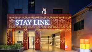 A hotel entrance with a 'STAY LINK' sign, a 'SAJA COFFEE' sign, and a 'CUSTOMER FOCUS' sign. - StayLink (Seoul)
