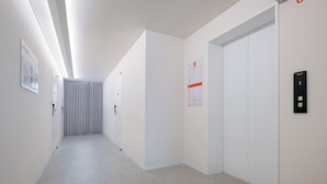 A modern hallway with white walls, a tiled floor, and an elevator with a digital display. - StayLink (Seoul)