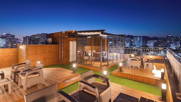 A rooftop terrace with outdoor furniture, a glass enclosure, and a city skyline view. - StayLink (Seoul)