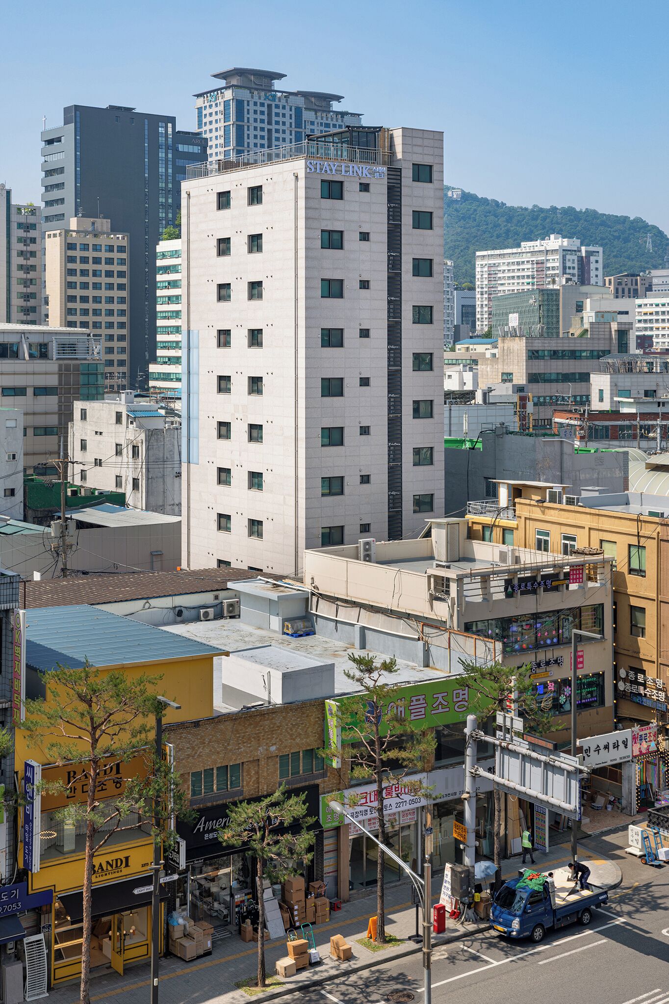 A cityscape with a prominent white building with 'STANLEY' signage, surrounded by various other buildings and a street with a blue truck.