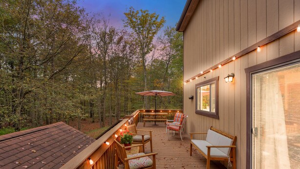 Un terrazzo in legno con mobili da esterno, luci decorative a catena e vista sugli alberi.
