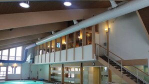 Una piscina interna con barriera in vetro, una scala e vista sul piano superiore.