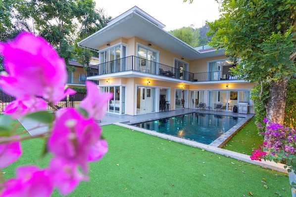 A two-story house with a swimming pool, a balcony, and a well-maintained lawn.