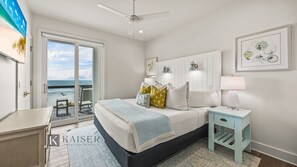 A bedroom with a bed, bedside tables, a ceiling fan, and a view of the ocean.