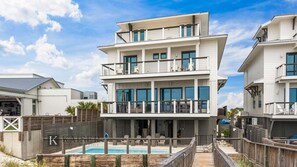 A multi-story beachfront property with a pool, balconies, and a wooden deck.