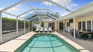 A covered swimming pool with lounge chairs and a dining area. - Sunny Marco Home with Heated Pool Near Beaches (Marco Island)