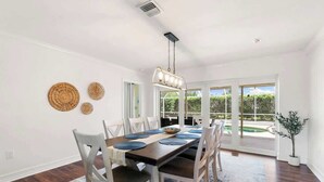 A dining area with a wooden table, white chairs, and a hanging light fixture. - Sunny Marco Home with Heated Pool Near Beaches (Marco Island)