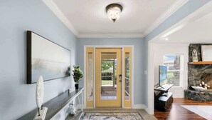 A hallway with a dark wood floor, a patterned rug, a framed artwork on the wall, a potted plant, and a stone fireplace. - Sunny Marco Home with Heated Pool Near Beaches (Marco Island)