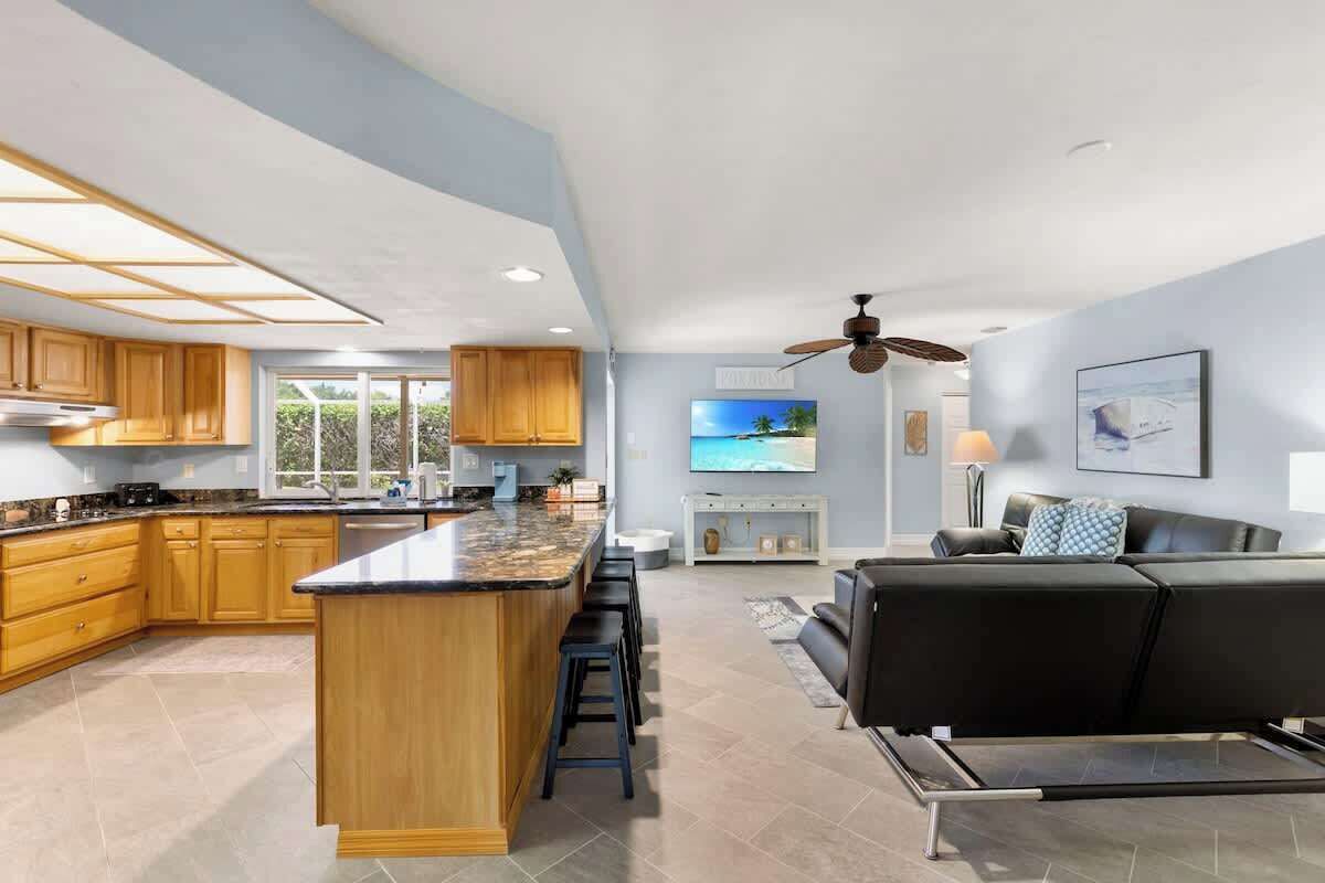 A spacious kitchen with wooden cabinets, a central island with bar stools, a dining area with a sofa and TV, and a ceiling fan.