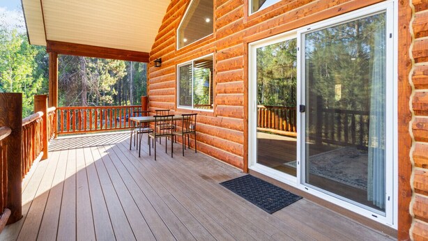 A wooden cabin with a deck, a dining area with chairs, and large sliding glass doors.
