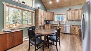 A kitchen with wooden cabinets, a dining table with chairs, a refrigerator, and a window with blinds.