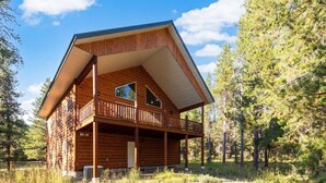 A log cabin with a balcony and a second-story window, surrounded by trees.