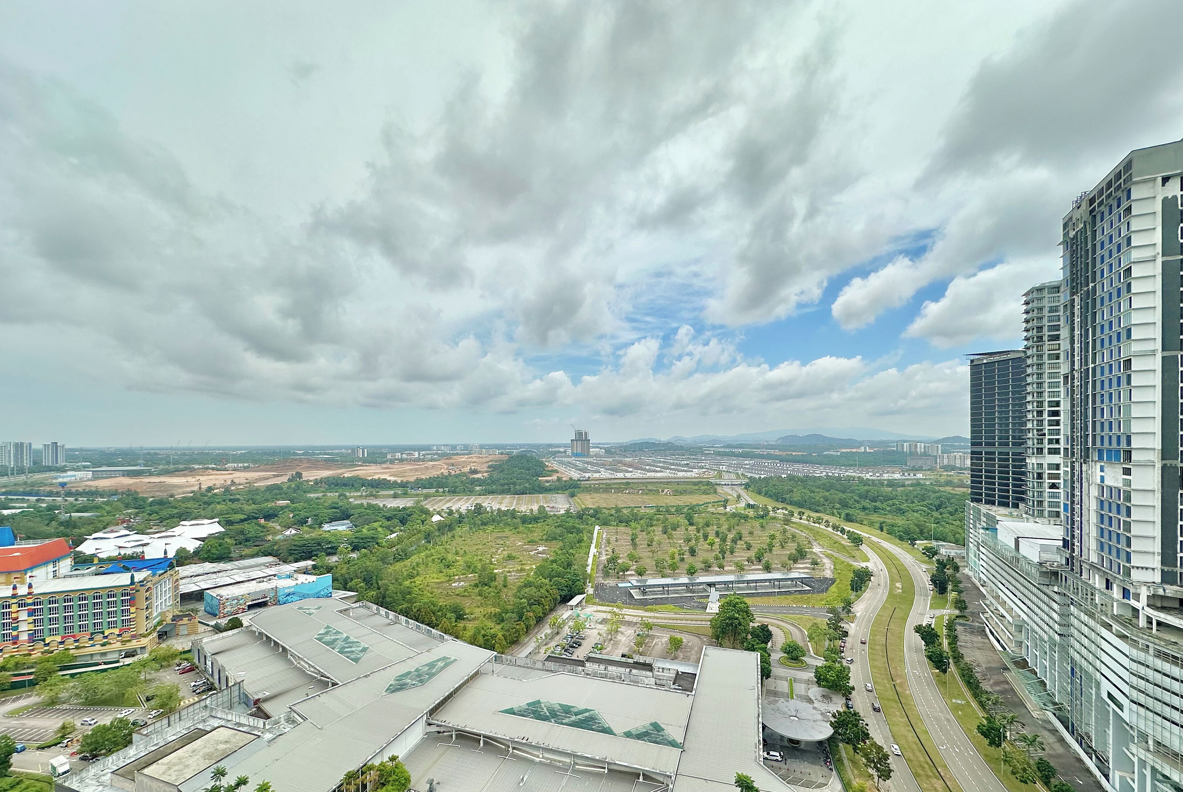 A high-rise building with a modern architectural design, surrounded by greenery and a curved road.