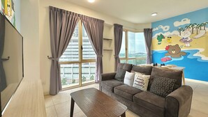 Una sala de estar con sofá, mesa de centro y ventanas grandes con cortinas.