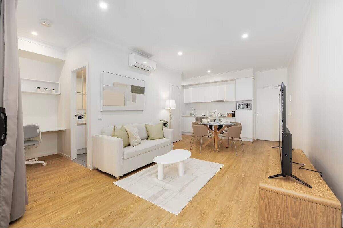 A modern, well-lit living room with a white sofa, a coffee table, and a TV on a stand.