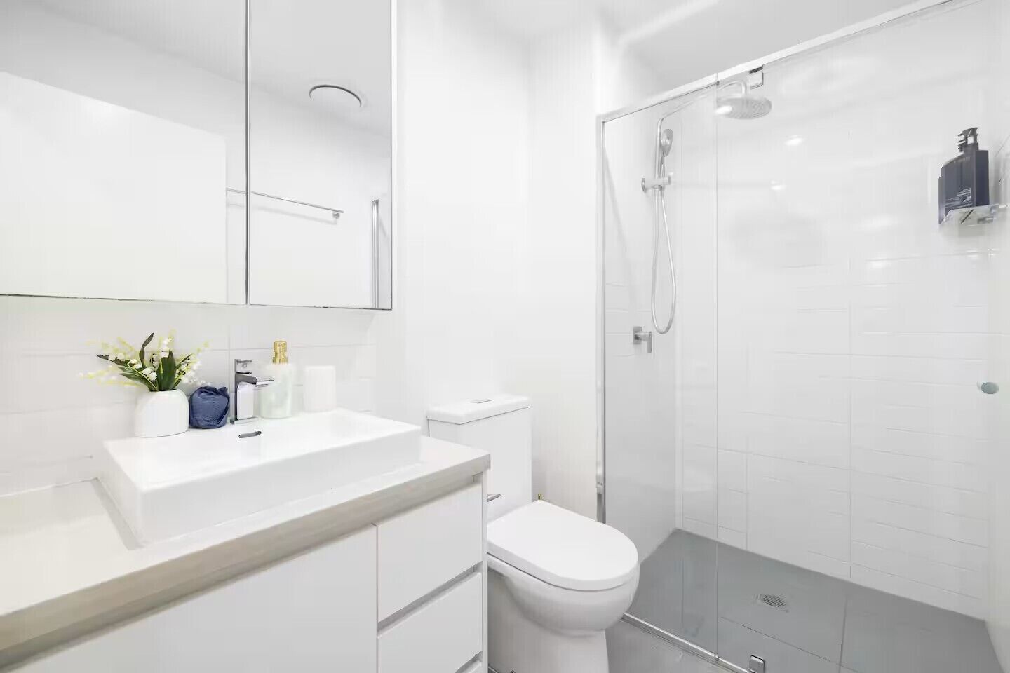A modern bathroom with a white sink, toilet, and glass-enclosed shower.