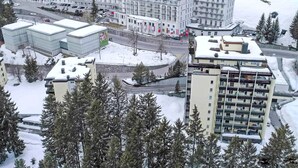 Un edificio grande de varios pisos con fachada simétrica, rodeado de terreno nevado y árboles.