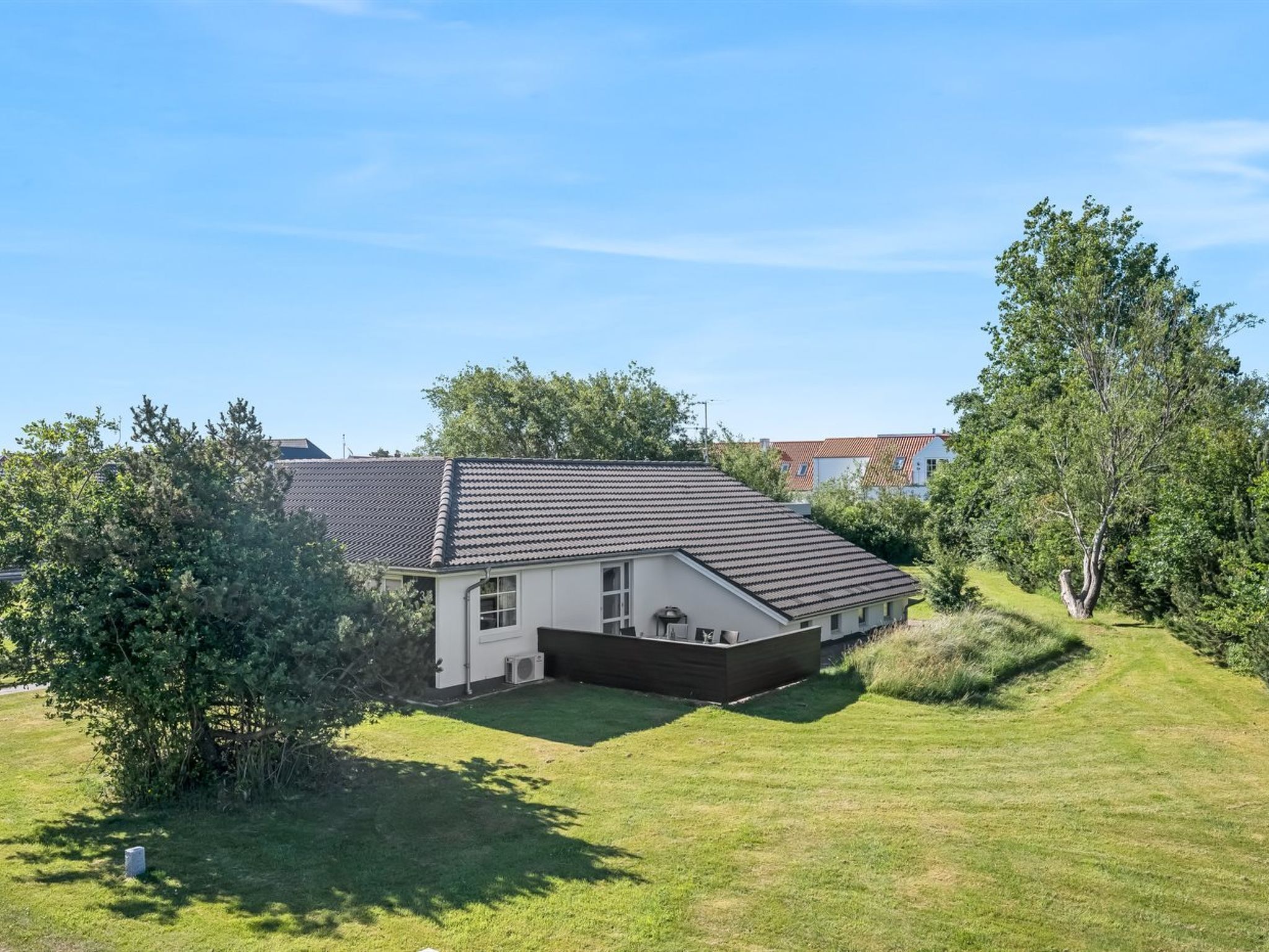 Une maison de plain-pied, dotée d’un toit en tuiles, entourée d’une pelouse bien entretenue et d’arbres.