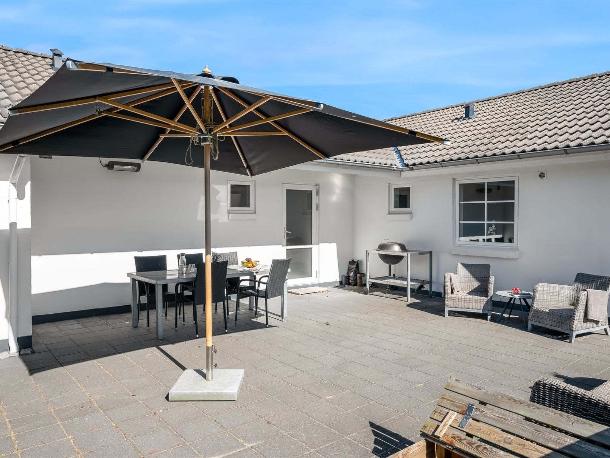 A patio with a table and chairs, a grill, and a large umbrella.