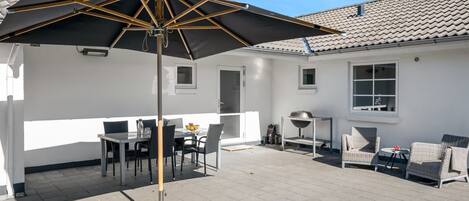 A patio with a table and chairs, a grill, and a large umbrella.