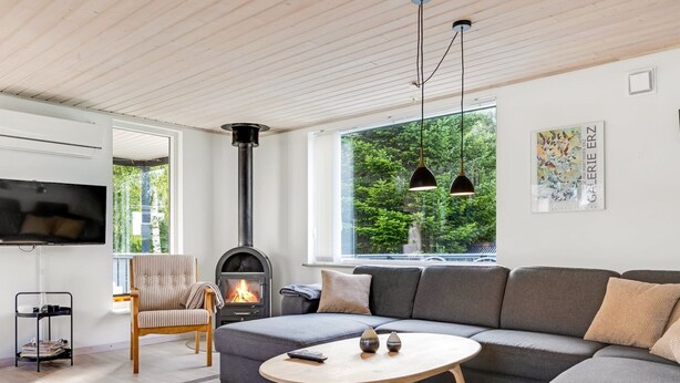 Una sala moderna con un amplio sofá seccional gris, una mesa de centro redonda, un sillón a rayas, una chimenea y un televisor montado en la pared.
