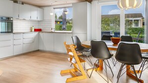 Una cocina moderna con armarios blancos, una mesa de comedor de madera con sillas negras, y un ventanal que ofrece vistas al exterior.