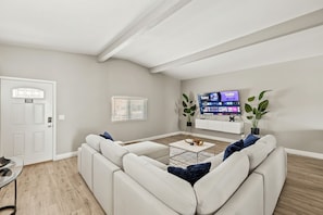 A modern living room with a white sofa, a coffee table, and a flat-screen TV mounted on the wall. - Private home with pool! Sleeps 16 people (Las Vegas)