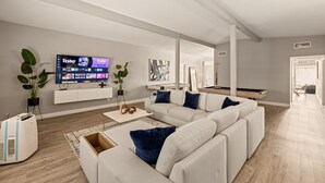 Ein modernes Wohnzimmer mit einem Ecksofa, einem Flachbildfernseher und einem Billardtisch.