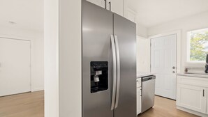 A modern kitchen with a stainless steel refrigerator, white cabinetry, and a built-in dishwasher.