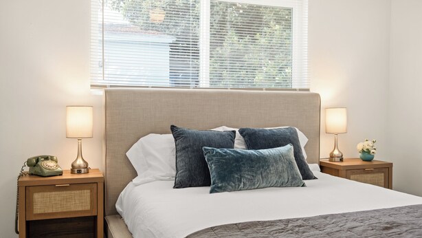 A neatly made bed with a beige headboard, two bedside lamps, and a vintage telephone on a wooden nightstand.