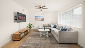 A modern living room with a flat-screen TV, a ceiling fan, a gray sofa, a coffee table, and a patterned rug.