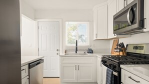 A modern kitchen with white cabinetry, a built-in dishwasher, a stainless steel stove, and a microwave above the stove.