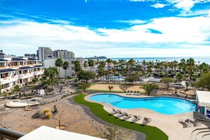 A resort with a large swimming pool, palm trees, and a view of the ocean.