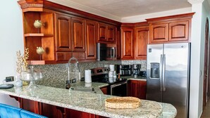 Una cocina con armarios de madera, encimeras de granito, electrodomésticos de acero inoxidable y taburetes de bar azules.