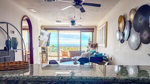 Una sala de estar moderna con un ventanal grande, un ventilador de techo y vista al océano.